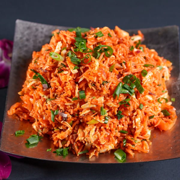 Close-up of a vibrant orange rice dish with shredded chicken and green onions on a dark plate.